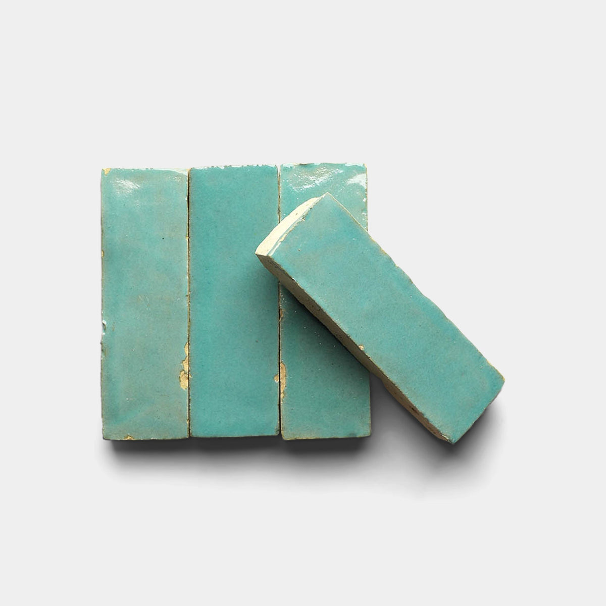Four Tulum 2x2 tiles by Zia Tile, featuring a glossy turquoise finish and worn edges, are arranged side by side on a white background with one tile slightly angled and overlapping the others.