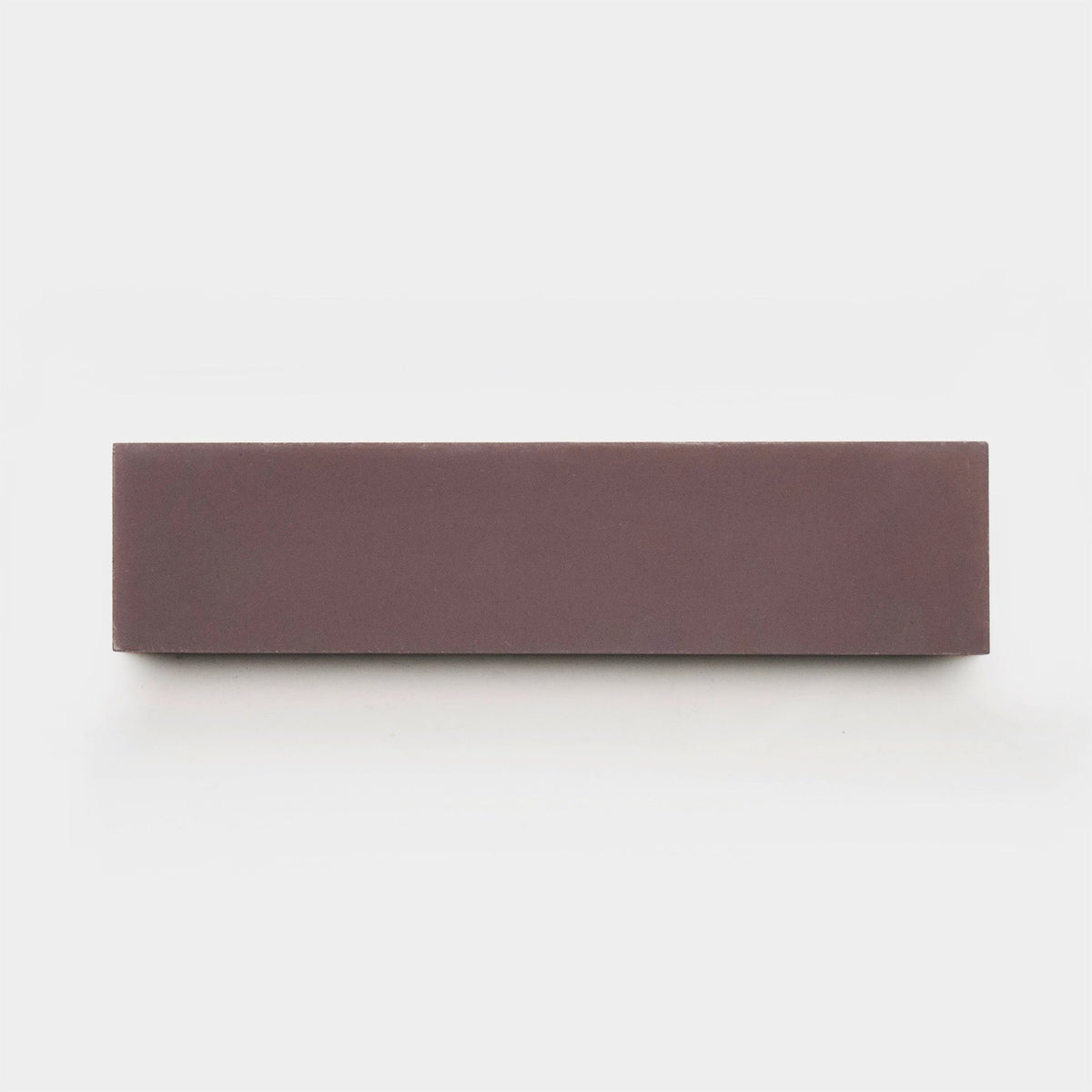 A rectangular Tyrian 2x8 sample from vendor-unknown, in a reddish-brown hue, lies on a plain white background—echoing the earthy tones seen in handmade cement tiles.