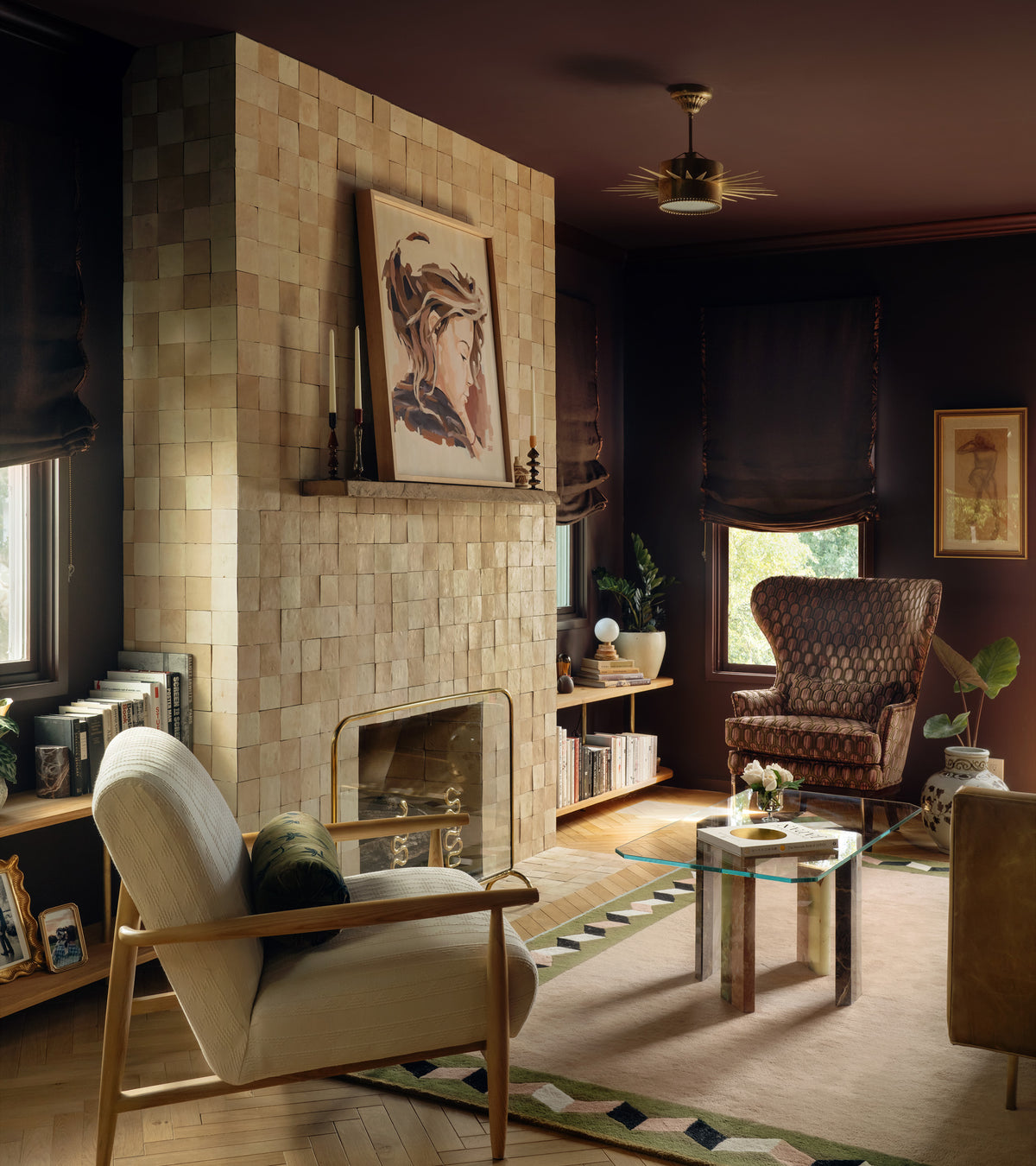 Cozy living room with a tiled fireplace featuring Zia Tile Unglazed Natural 4x4 tiles, an armchair, patterned rug, framed artwork, and bookshelves lining the walls as sunlight filters through window shades for a warm ambiance.