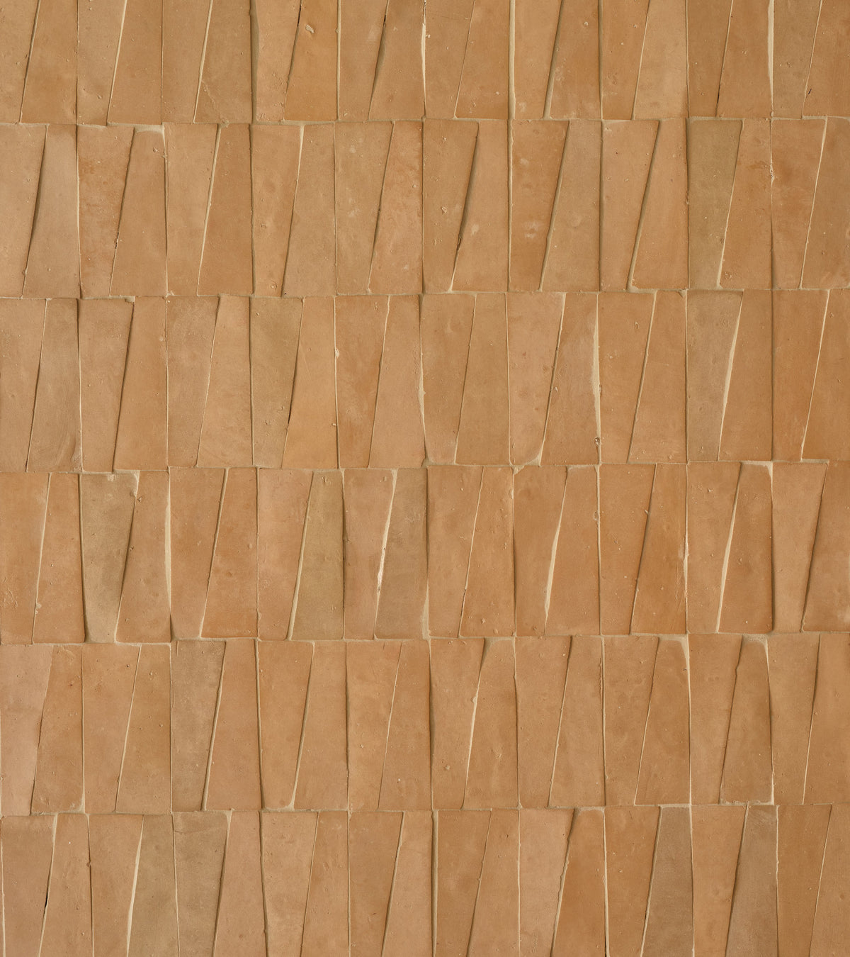 A close-up of a wall featuring Zia Tile's Unglazed Natural Trapezoid tiles in a staggered, overlapping layout, showcasing varied sizes and natural shades for a rich, organic look.