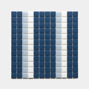 A grid of small square tiles in Union Damascus, Tranquil Blue, and Paperwhite by Zia Tile forms vertical stripes of dark blue, light blue, and white on a plain light background.