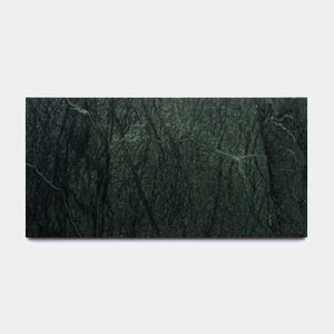 The Verde Alpi 12x24 by Zia Tile is a rectangular slab of dark green marble with natural veins running diagonally, reminiscent of a handmade tile. It is shown against a plain white background.
