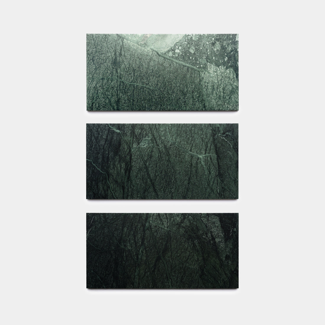 Three Verde Alpi 12x24 marble tiles by Zia Tile, each featuring unique dark green veining, are displayed vertically against a plain white background.