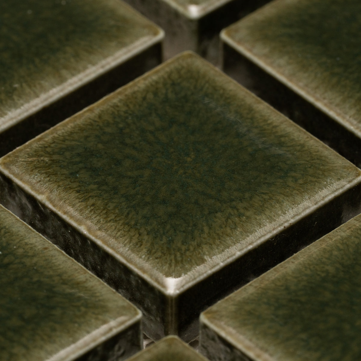 Close-up of Zia Tile’s Vetiver 1x1 tiles—glossy, dark green ceramic squares with textured surfaces and slightly raised edges arranged in a grid pattern.