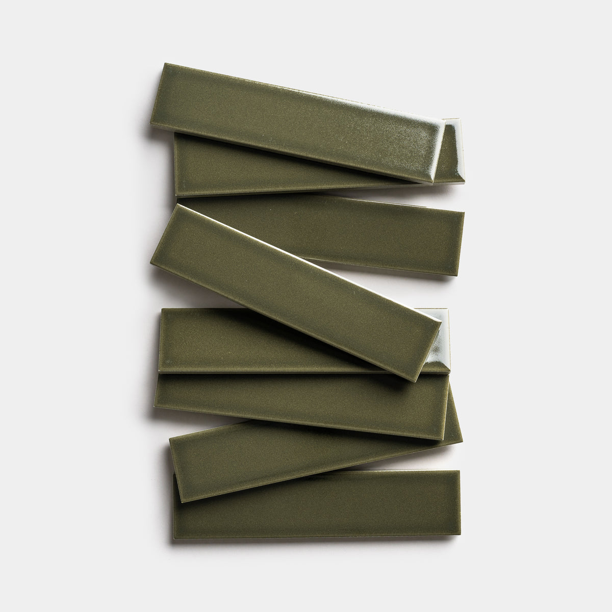 Seven glossy, rectangular Vetiver 2x8 tiles by Zia Tile in olive green are arranged in a loose, overlapping zigzag on a plain white background.