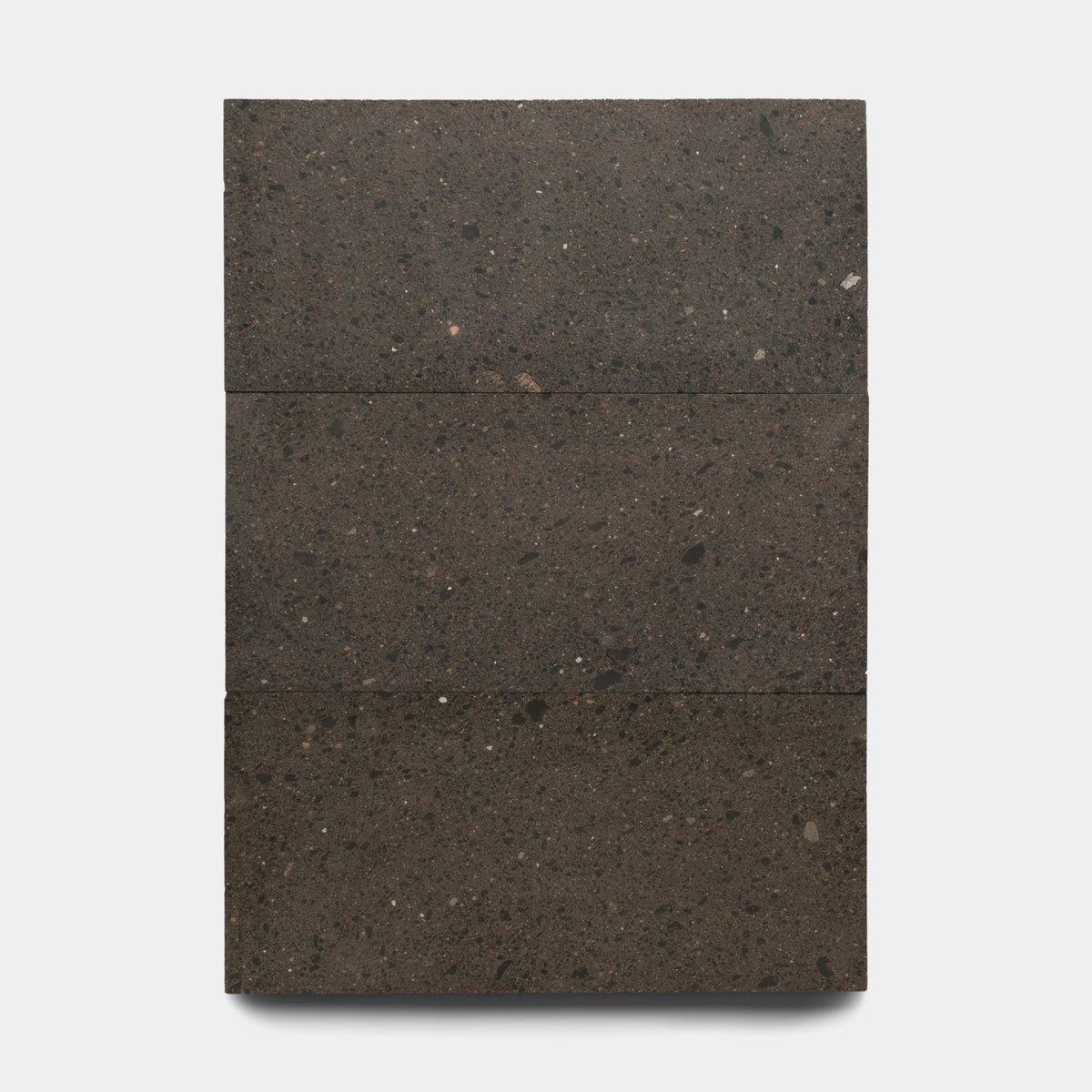 The Volcan 12x24 by Zia Tile is a rectangular block of three stacked, dark gray Mexican Cantera stone slabs with a speckled, slightly rough texture, shown against a plain white background.