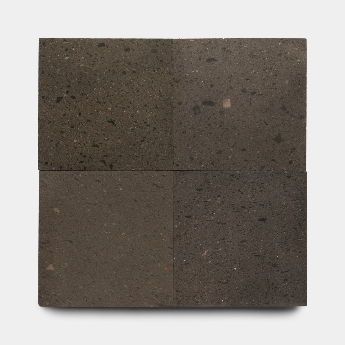 Four Volcan 24x24 tiles by Zia Tile are arranged in a 2x2 grid on a white background. Each dark brown volcanic stone tile features unique textures and speckling, giving them an earthy, natural appearance.