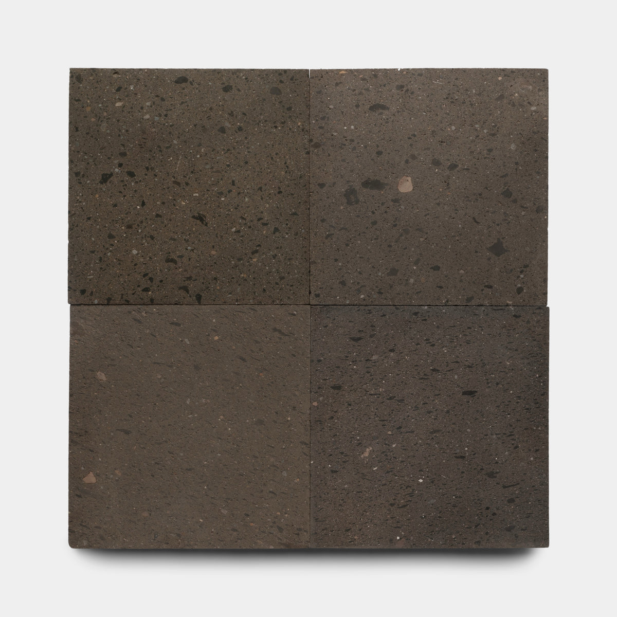 Four Volcan 24x24 tiles by Zia Tile are arranged in a 2x2 grid on a white background. Each dark brown volcanic stone tile features unique textures and speckling, giving them an earthy, natural appearance.