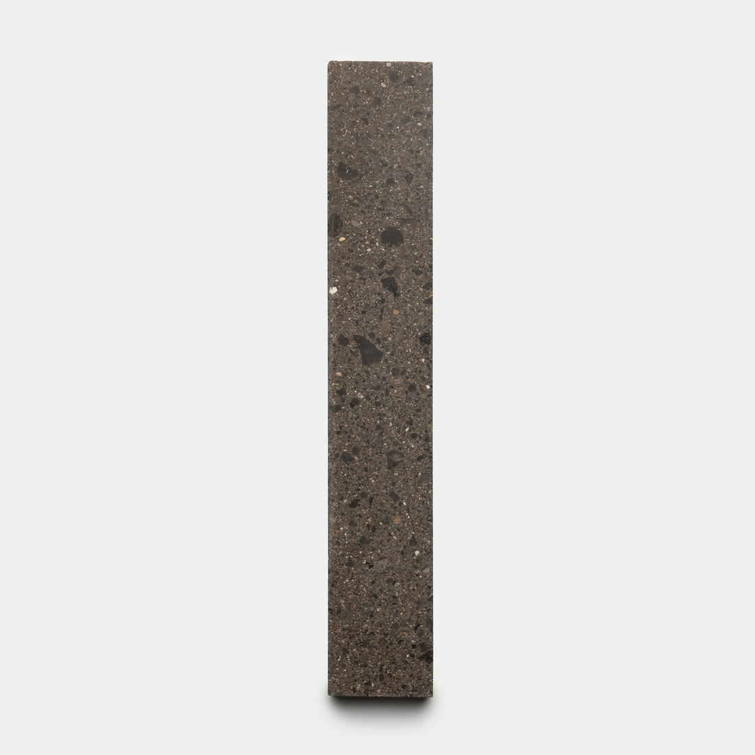 The Volcan 2x12 by Zia Tile is a tall, rectangular tile of dark speckled stone, standing upright against a light gray background.