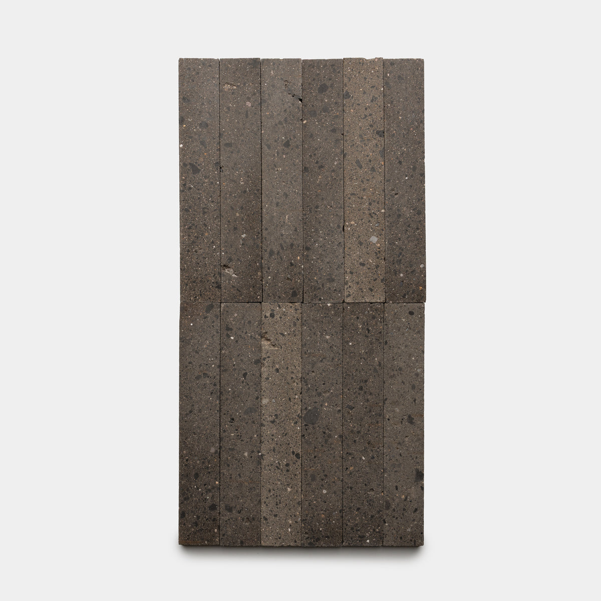 Sixteen Volcan 2x12 tiles by Zia Tile, dark gray with a speckled texture, are arranged in four rows on a white background.