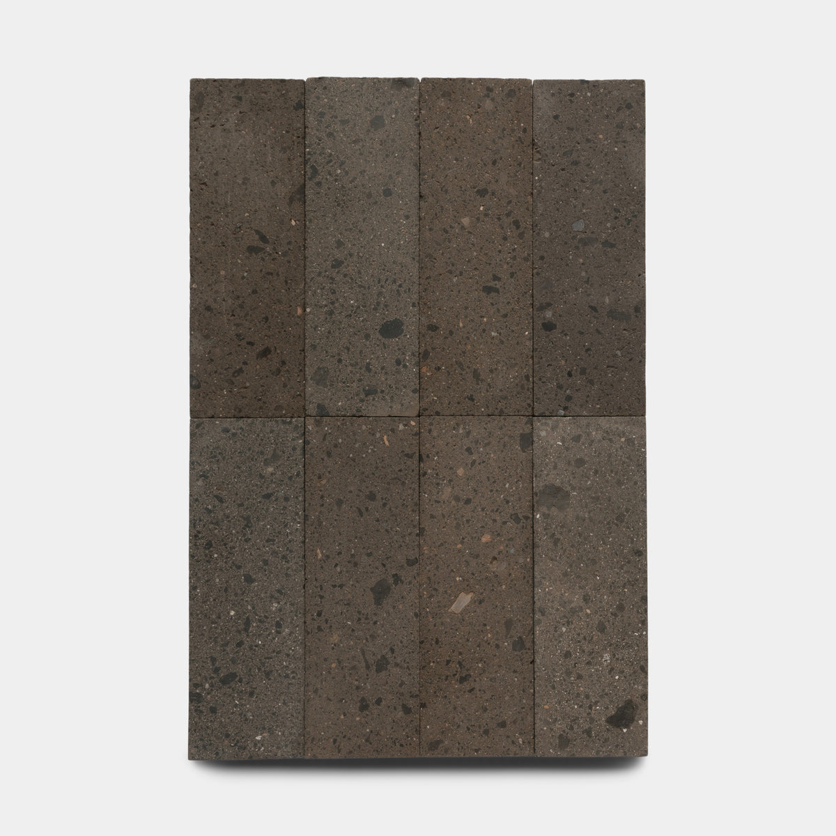 Zia Tile's Volcan 4x12 tiles, crafted from natural volcanic stone, are arranged in a neat 3x3 grid on a plain white background. The dark gray tiles showcase a rough, porous texture with small specks and subtle color variations.