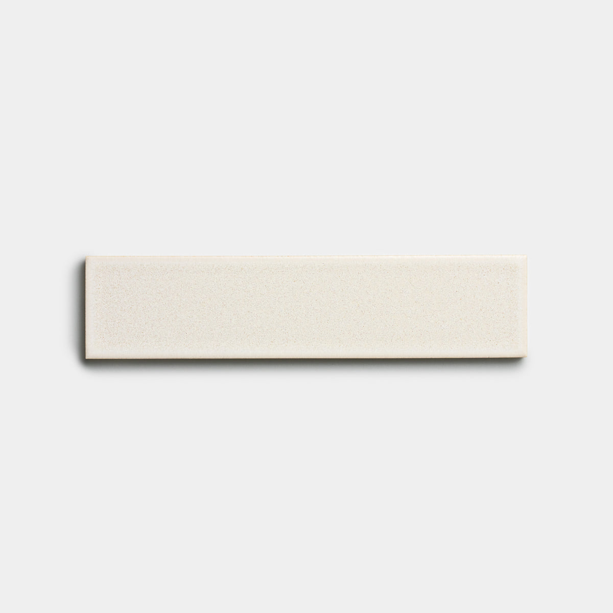 The Wool 2x8 ceramic tile by Zia Tile, featuring a rectangular shape and smooth matte cream finish, is centered on a plain light gray background.