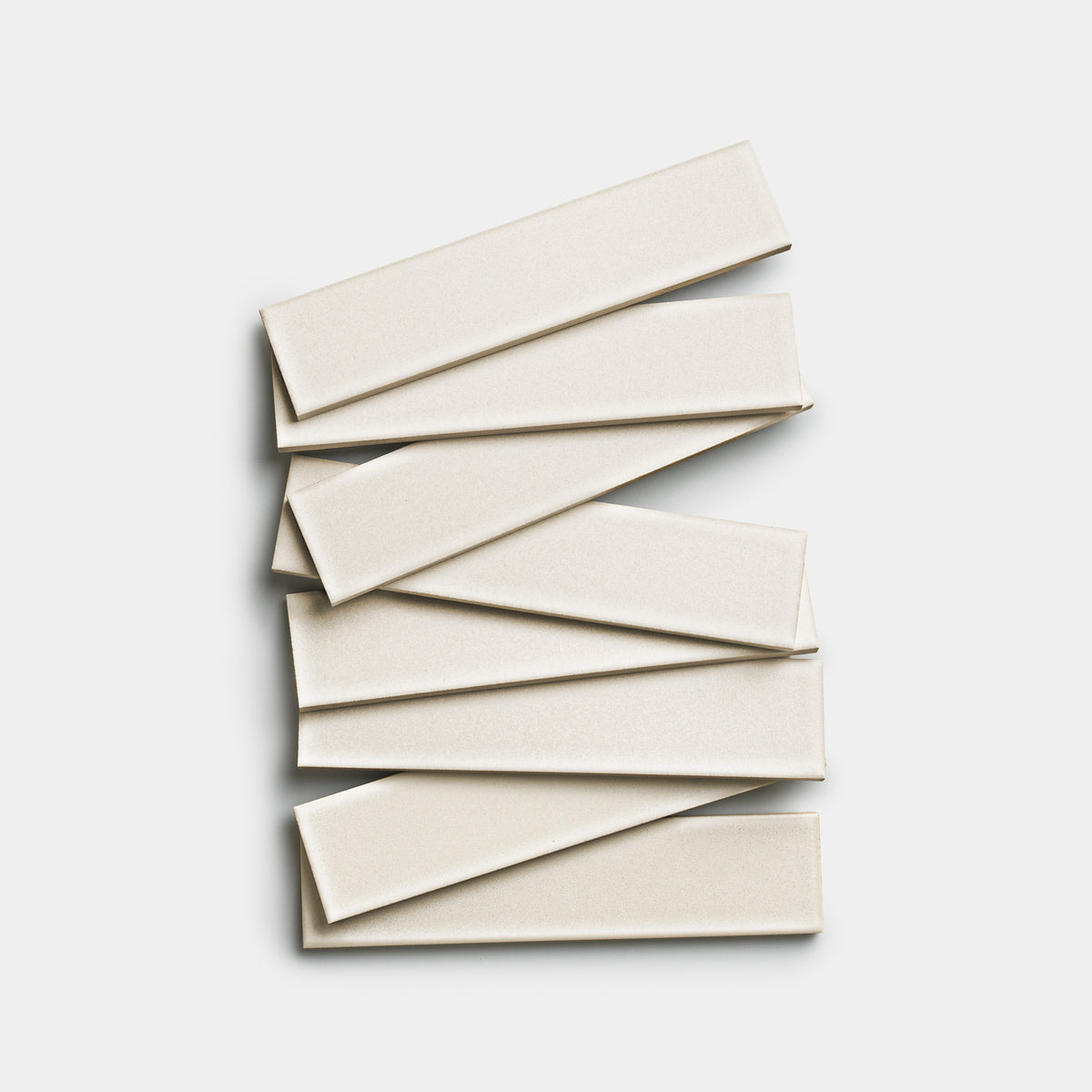 Seven Wool 2x8 off-white rectangular ceramic tiles by Zia Tile are stacked in a staggered, overlapping arrangement on a plain white background.