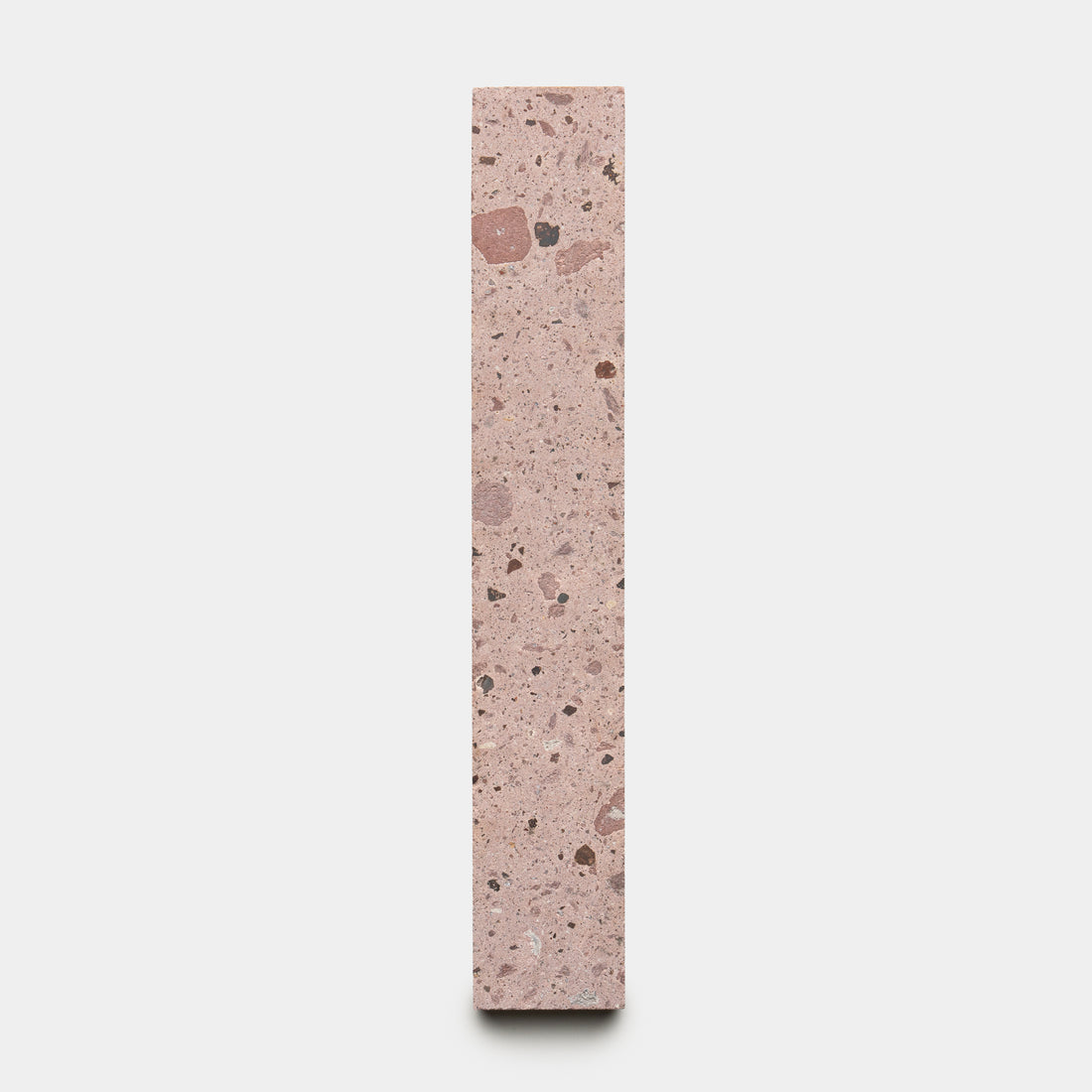 The Yuma 2x12 by Zia Tile is a tall, rectangular block of pink terrazzo with mixed dark and light stone specks, shown upright against a plain white background.