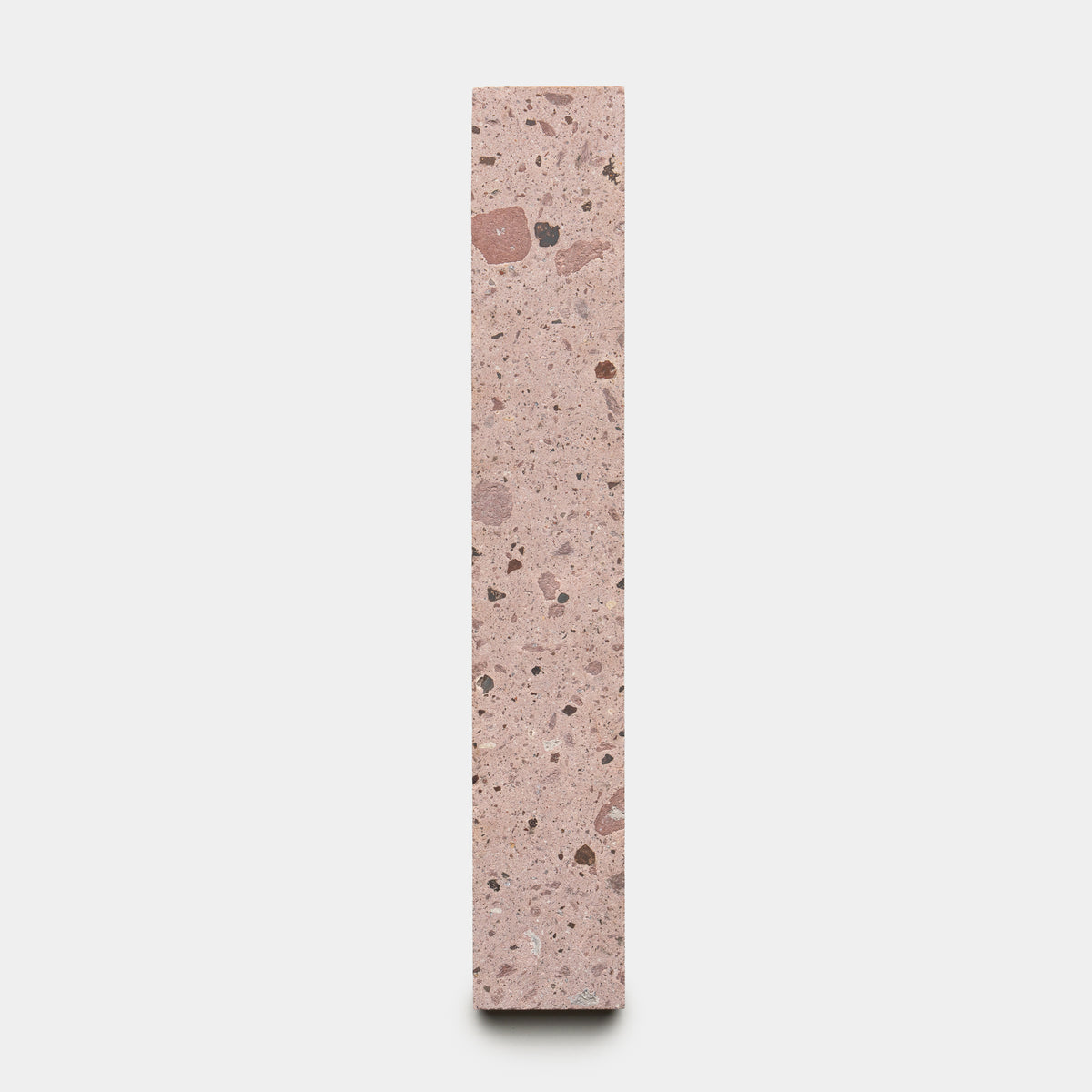 The Yuma 2x12 by Zia Tile is a tall, rectangular block of pink terrazzo with mixed dark and light stone specks, shown upright against a plain white background.