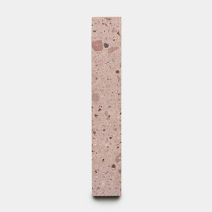 The Yuma 2x12 by Zia Tile is a tall, rectangular block of pink terrazzo with mixed dark and light stone specks, shown upright against a plain white background.