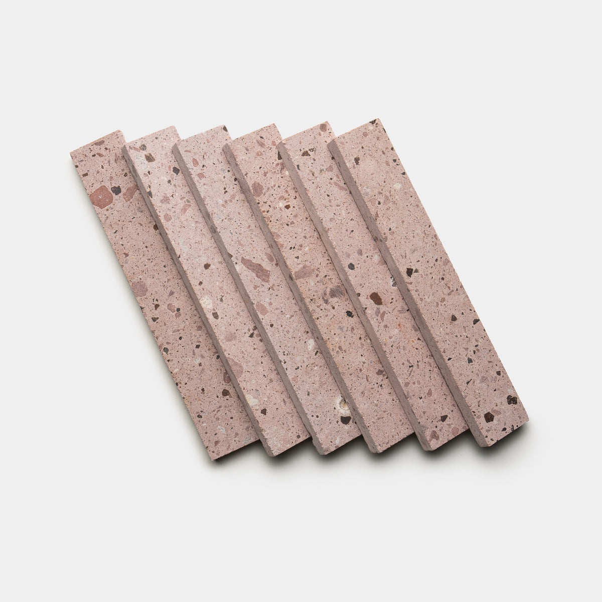 Six rectangular Yuma 2x12 terrazzo tiles by Zia Tile, in speckled pink, are arranged diagonally and slightly overlapped on a white background.