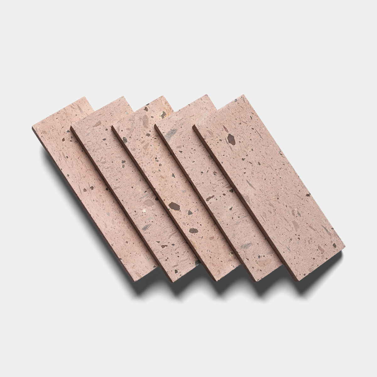 Five Yuma 4x12 terrazzo tiles by Zia Tile, rectangular with a pinkish tone and scattered dark fragments, are displayed in a slightly fanned-out pattern on a light background with soft shadows.