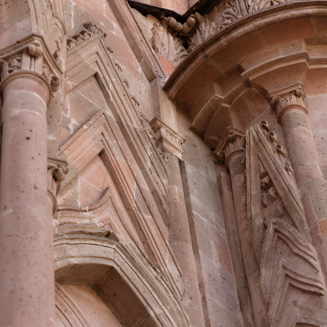 Detailed close-up of a pink stone Gothic-style building facade, showing pointed arches, ornate carvings, columns, and intricate masonry details.