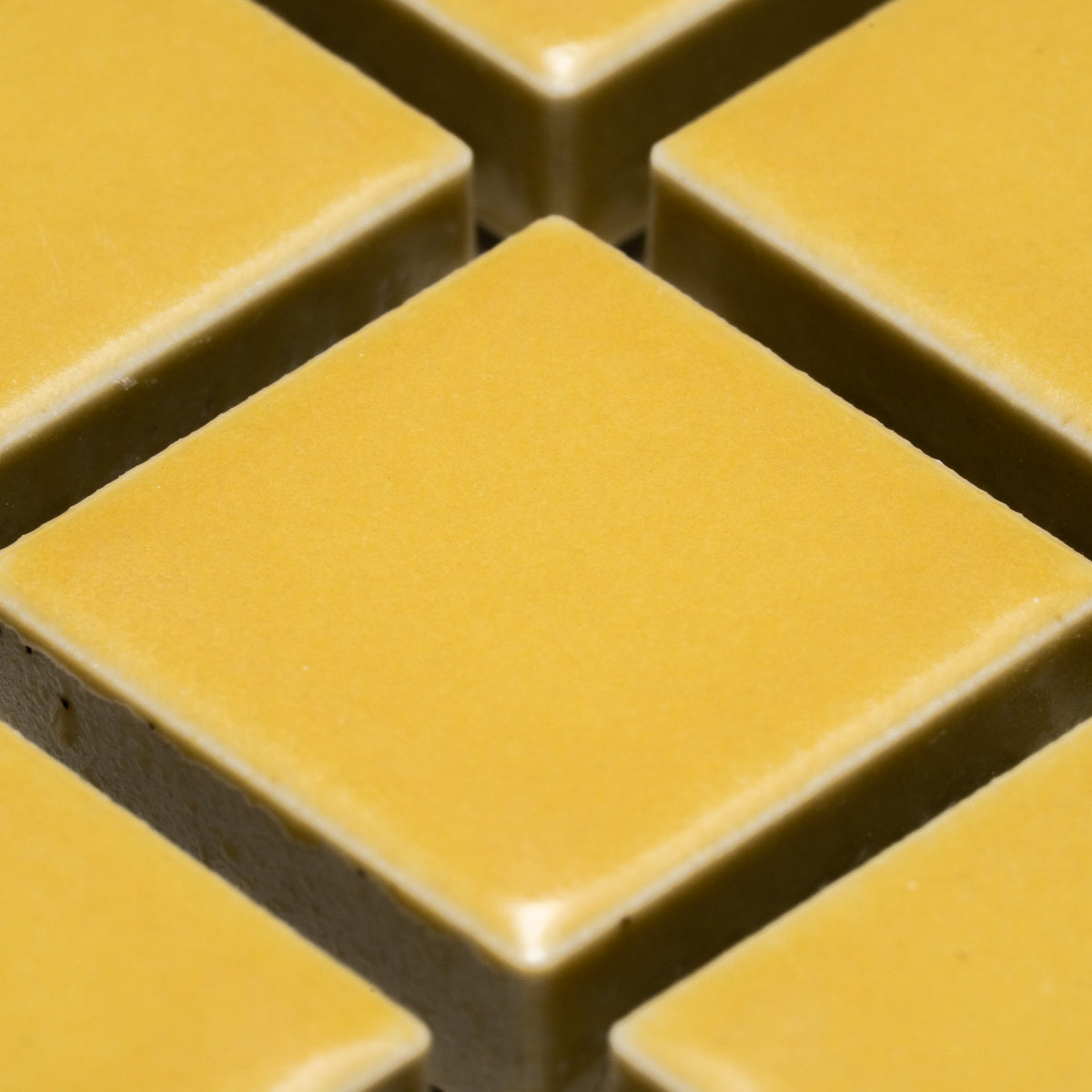 Close-up of Yuzu 1x1 tiles by Zia Tile, featuring yellowish-gold square shapes with beveled edges and a smooth, matte finish arranged in a grid pattern.