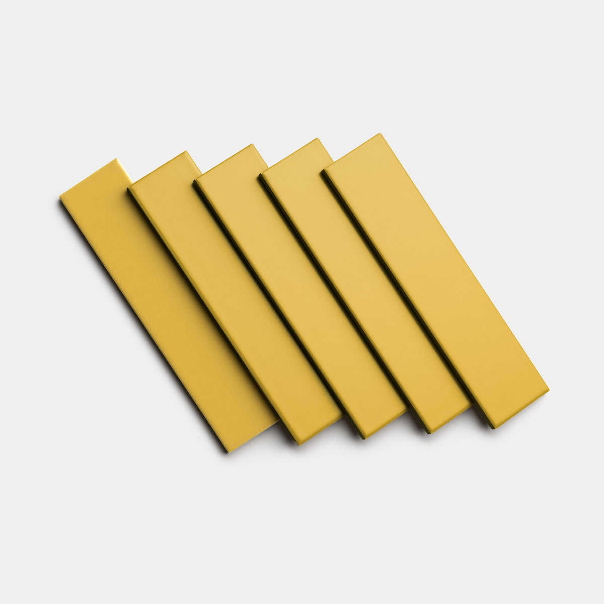 Five Yuzu 2x8 rectangular tiles by Zia Tile in a yellow-gold shade are arranged with slight overlap in a diagonal pattern against a plain white background.