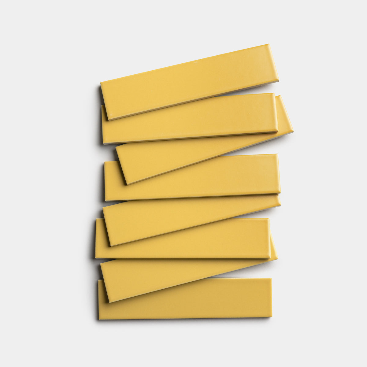 Seven rectangular, smooth, yellow Zia Tile Yuzu 2x8 tiles are stacked in a slightly offset, overlapping arrangement on a white background.