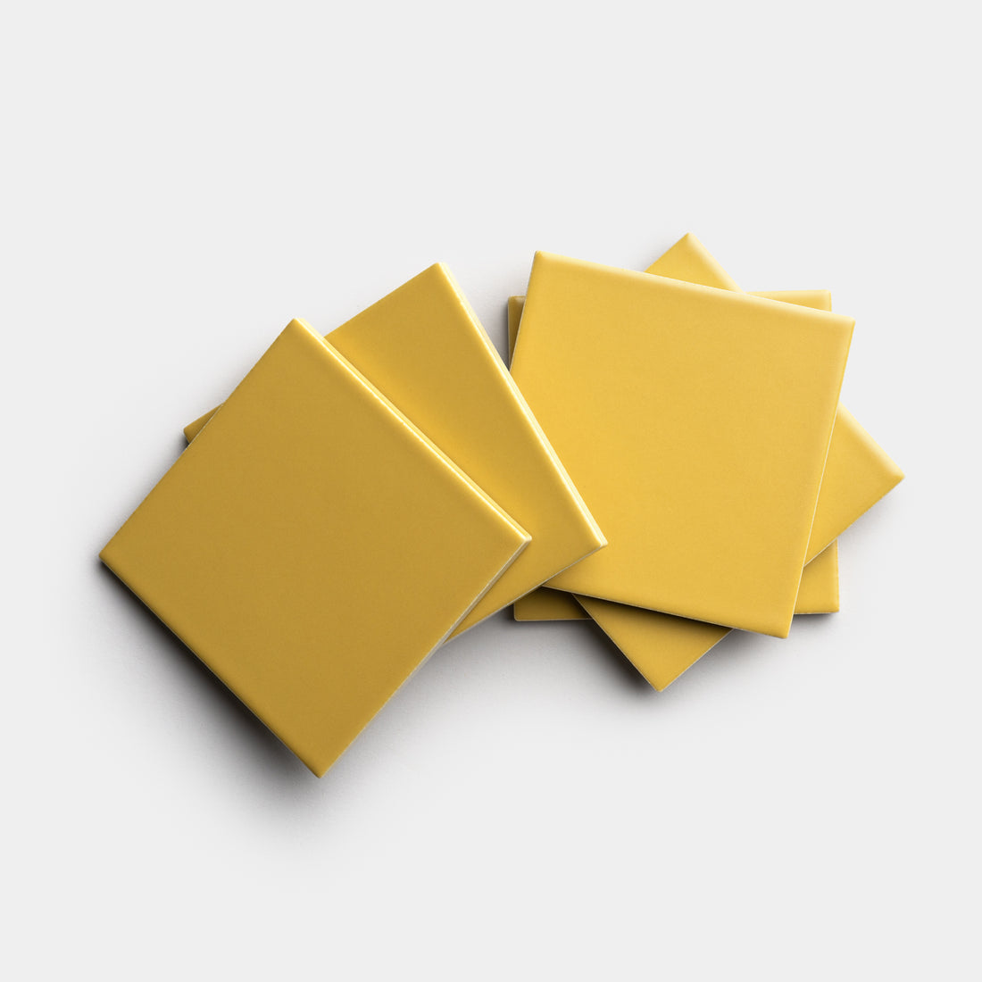 Five Yuzu 4x4 yellow square tiles by Zia Tile are arranged in a slightly overlapping, fanned-out pattern on a plain white background.