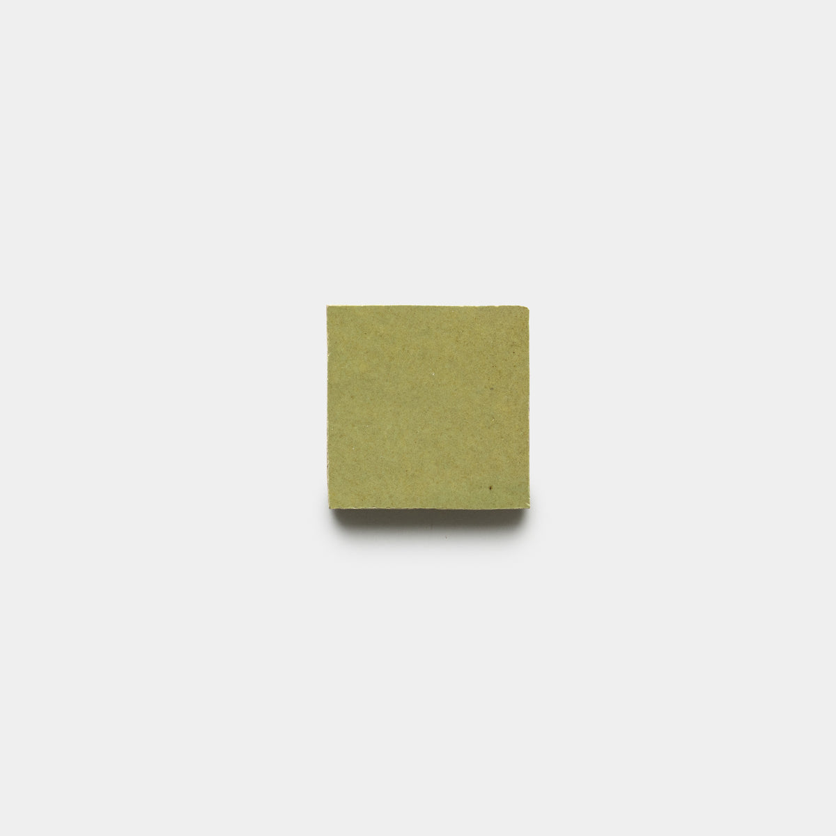 A single Za'atar 2x2 tile by Zia Tile, in a greenish-brown shade, is placed on a plain white background and viewed from above.