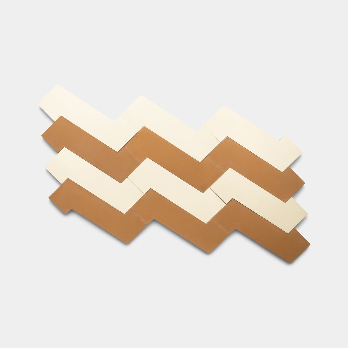 Zia Tile’s Zig Zag Bone + Saddle, Sample features a zigzag pattern of rectangular handmade tiles in alternating cream and light brown, arranged diagonally on a plain light gray background.