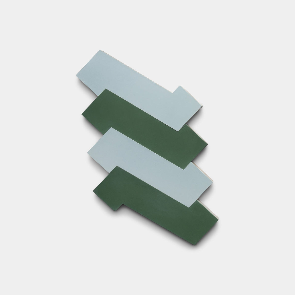Three interlocking Zig Zag Hailstone + Noble Green tiles from Zia Tile, in sage green and light blue, are arranged in a zigzag on white, showcasing the distinctive beauty of handmade tile.