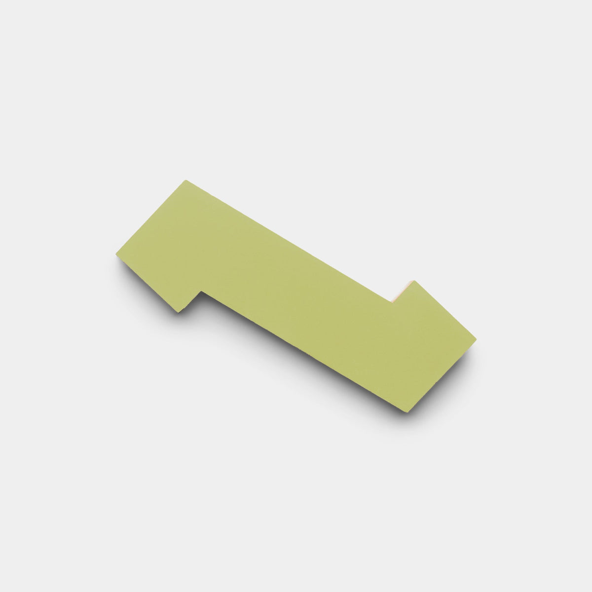A flat, light green geometric shape resembling a stylized arrow points left on a white background, showcasing the Zig Zag Lemongrass + Mustard tile sample from Zia Tile.