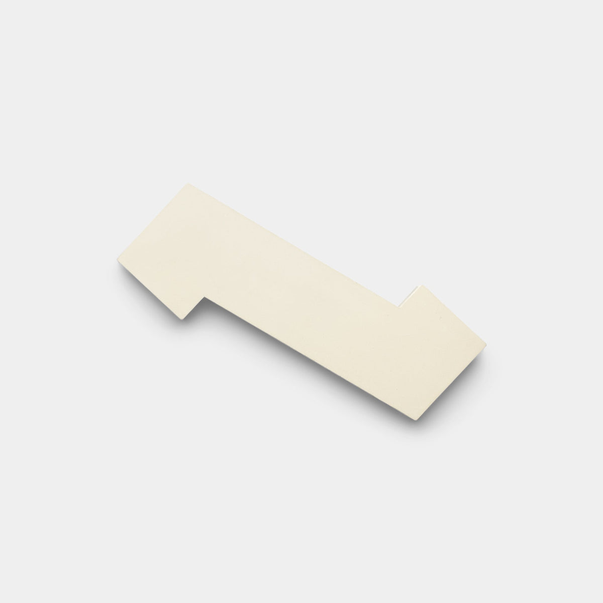 A sample of Zig Zag White + Bone by Zia Tile is a flat, off-white handmade tile with angular edges and a notch on one side, shown on a plain white background.