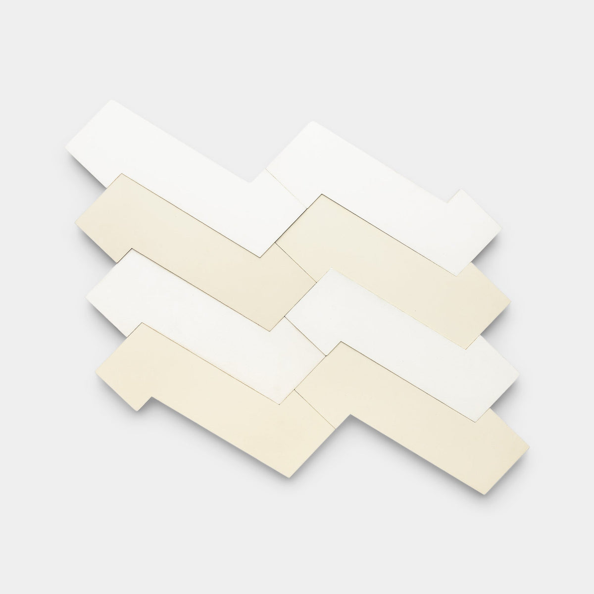 Six interlocking Zig Zag White + Bone tiles by Zia Tile feature irregular geometric shapes with right-angle extensions, arranged in a staggered zigzag pattern on a plain light background.
