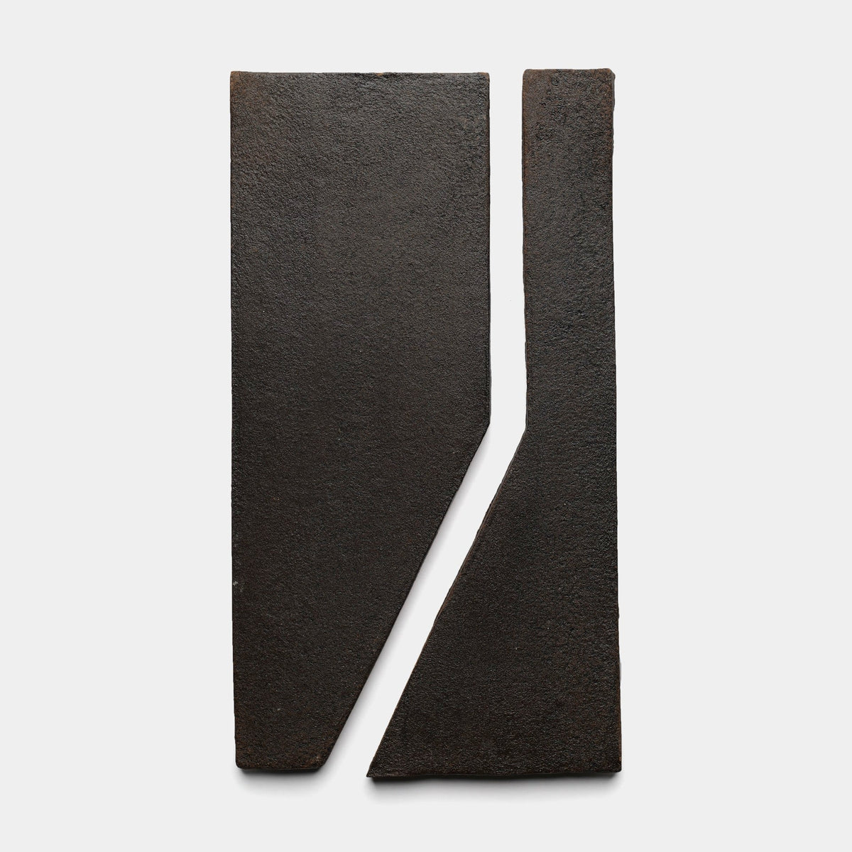 Two dark, rectangular Zocalo + Oscura samples by Zia Tile stand vertically side by side with a diagonal split between them, forming an abstract geometric composition on a white background.