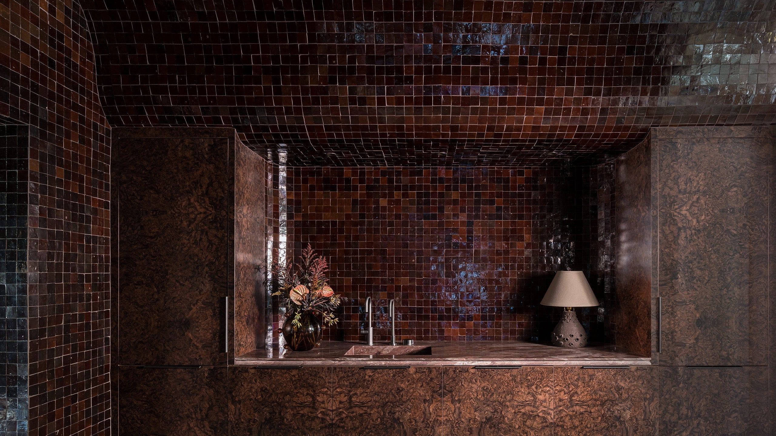 Decorative interior with mosaic tiles and a small table with a lamp and flowers.