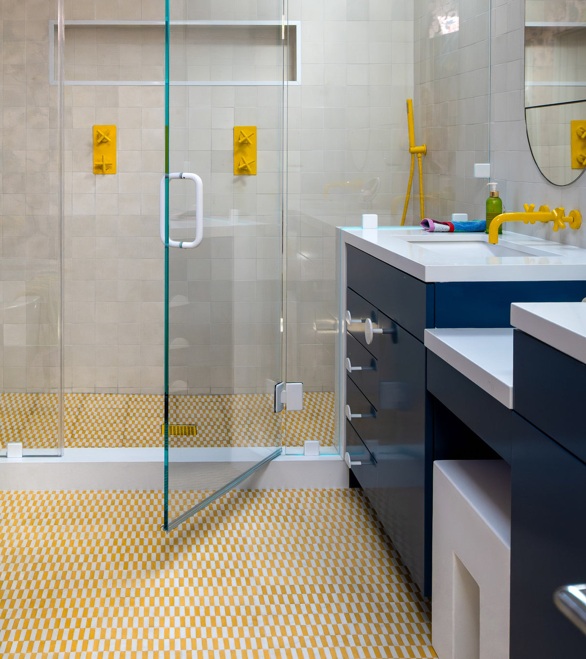Modern bathroom featuring a glass shower door, yellow fixtures, blue cabinetry, and a white countertop. The Rialto Cadmium 4x8 tile by Zia Tile brings brightness and contemporary flair to the floor, reminiscent of a stylish backsplash.