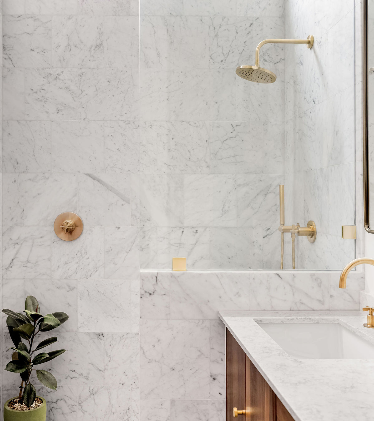 A handcrafted Carrara 12x12 tile shower wall and matching vanity countertop with brass fixtures.