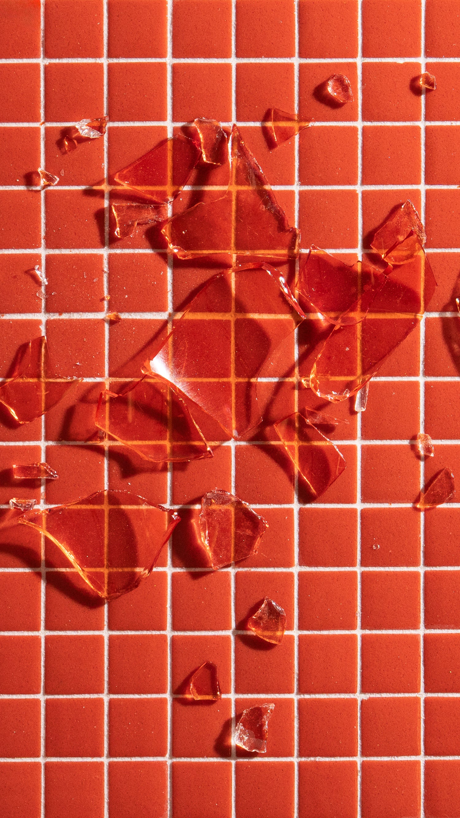 Shattered pieces of transparent red glass scattered on a red tiled surface with white grid lines.