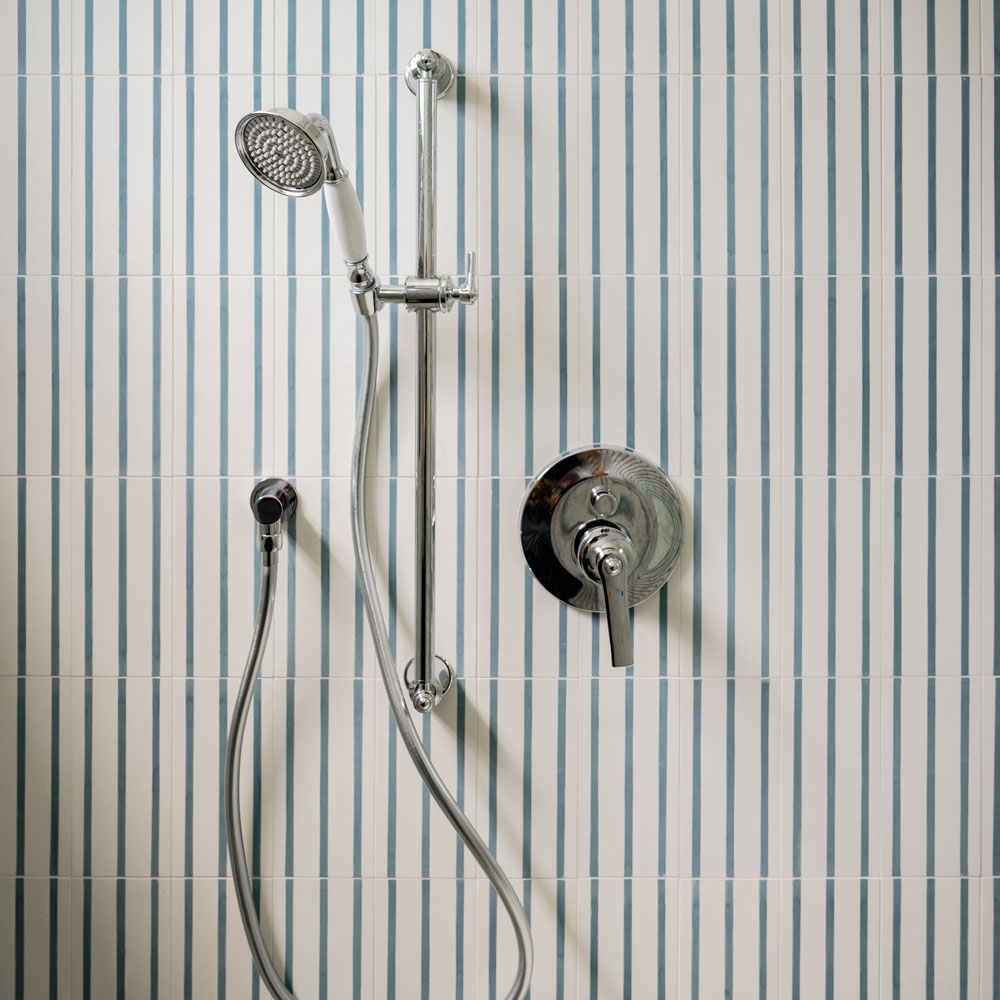 A modern shower with a handheld showerhead, chrome fixtures, and a control handle mounted on a wall with vertical blue and white striped tiles.
