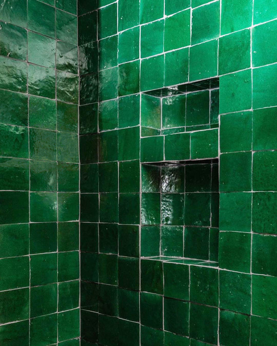 A corner wall covered with shiny, uneven green ceramic tiles featuring two built-in rectangular niches. The grout lines between the tiles are visible and slightly irregular.