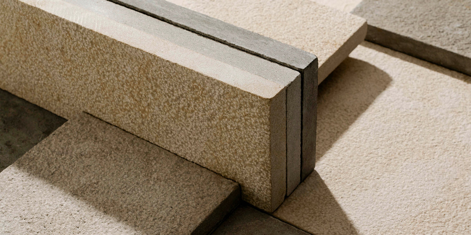 Close-up of textured beige and gray concrete blocks arranged in a geometric pattern, with light and shadow creating angular shapes across the surfaces.