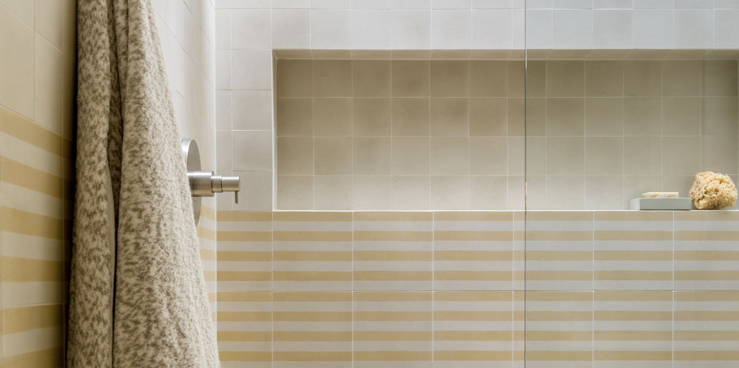 A shower with beige and white horizontal striped tiles, a silver faucet, a textured towel hanging, and a recessed shelf holding a sponge and a small soap dish.