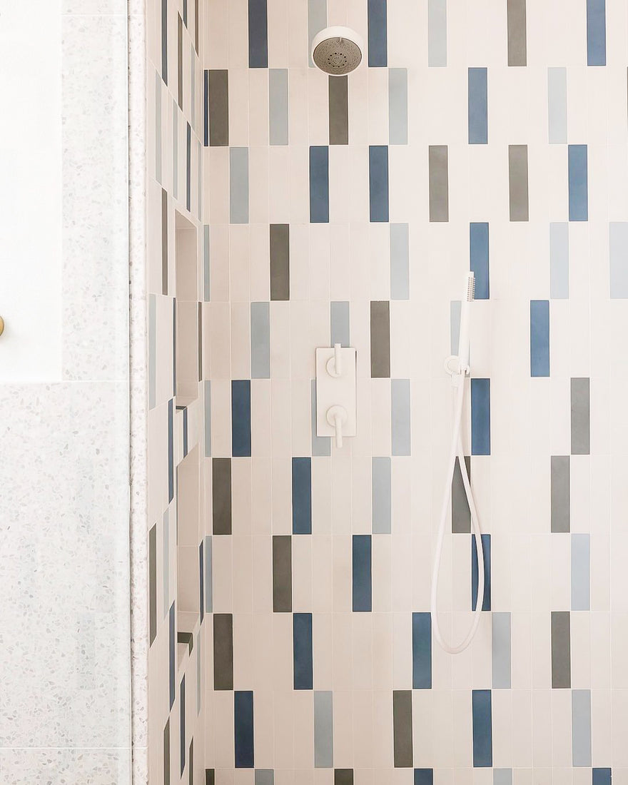 A modern shower with a wall of rectangular tiles in shades of blue, gray, and white, featuring a rainfall showerhead and a handheld shower wand with white fixtures.